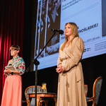 Prelegentka pokazu oraz Joanna Bojczuk Członek Zarządu Województwa stojące na scenie, w tle pokaz filmu