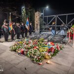 Uroczystość pod bramą z tablicami i wieloma wieńcami oraz uczestnikami w mundurach i z flagami